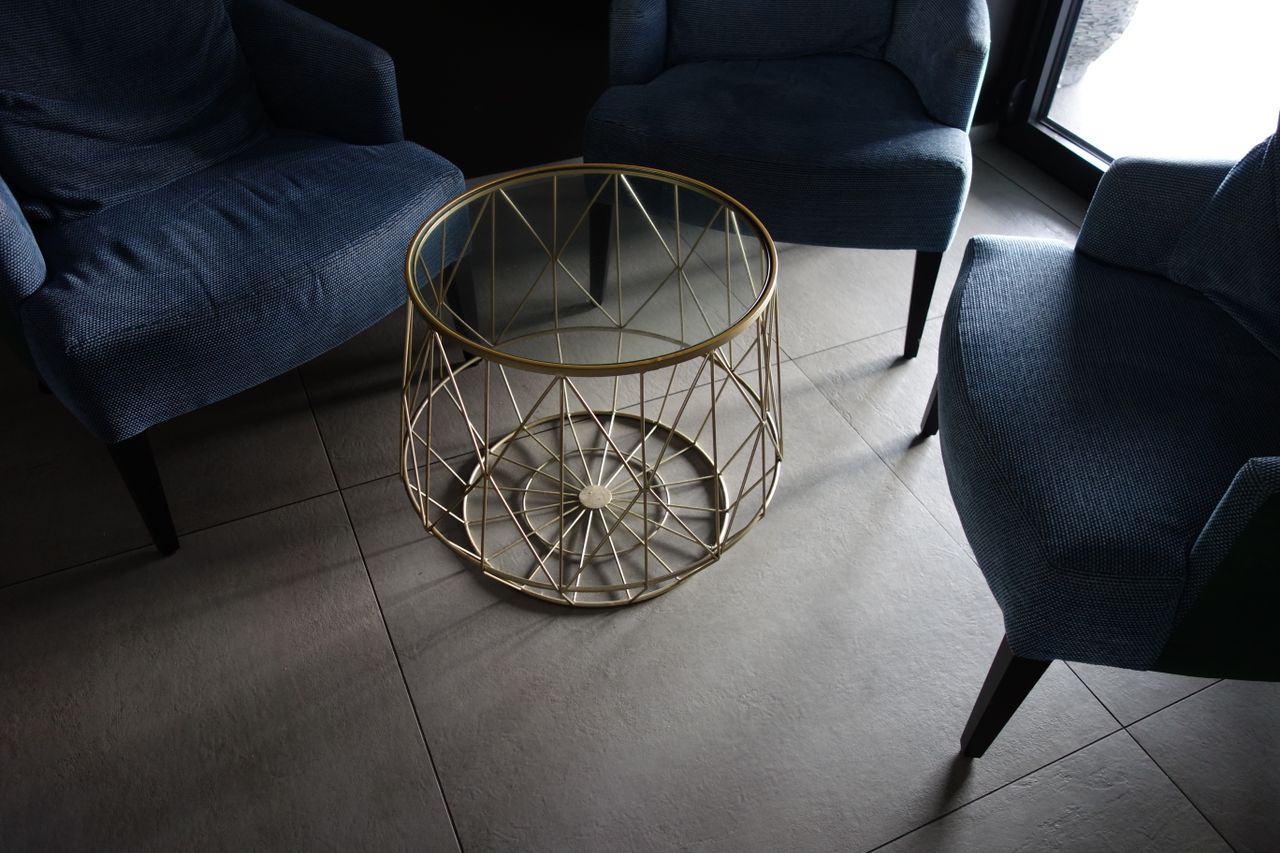 Stylish indoor lounge featuring blue armchairs around a glass-top metal table on tiled flooring.
